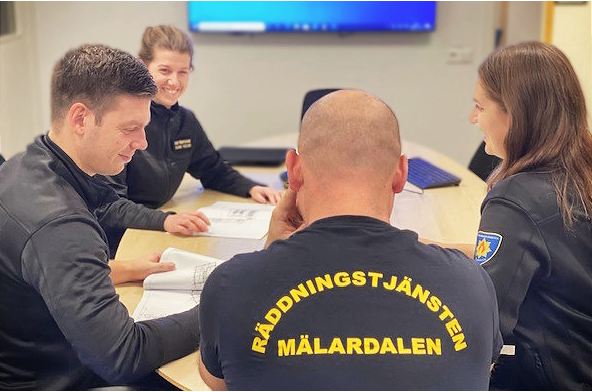 Fyra brandingenjörer från Räddningstjänsten Mälardalen sitter vid ett bord och arbetar.